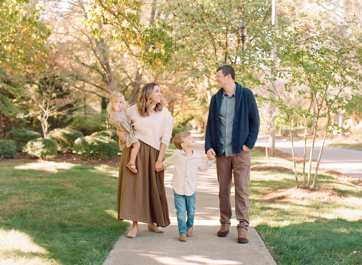 Family holds hands and walks down a side walk during a family portrait session in downtown Wake Forest. Family walking during their family portrait session in Wake Forest, NC. Photographed by Raleigh family photographer A.J. Dunlap Photography.
