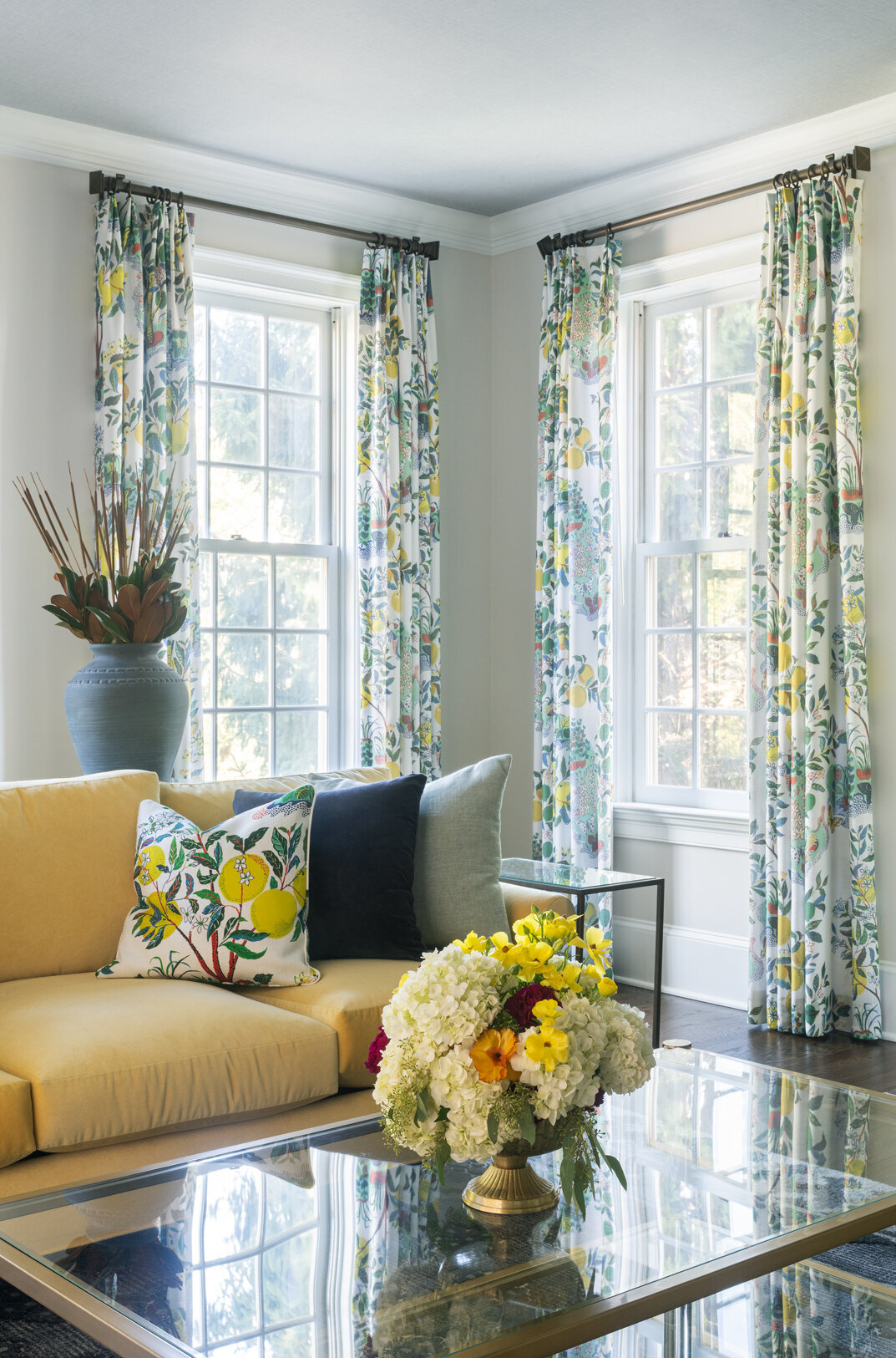 living room with a glass coffee table, yellow sofa and floral patterned curtains