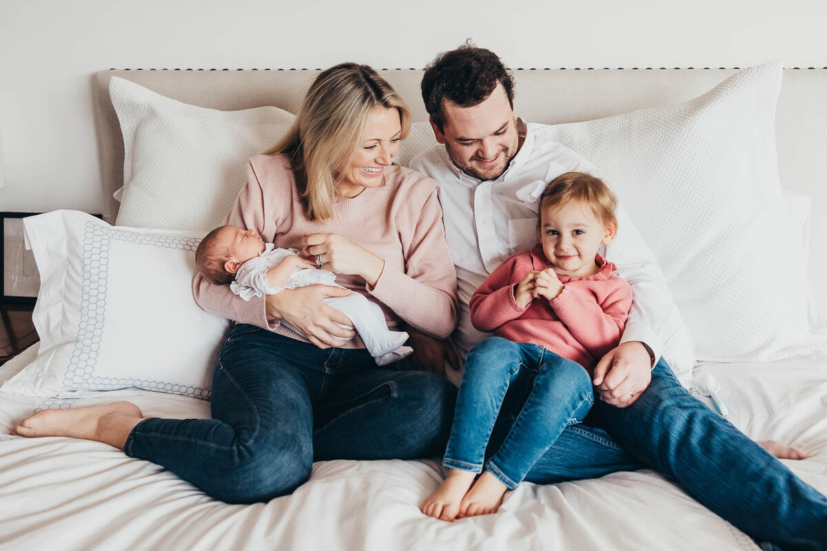 a family of four sit together on their bed in their del mar home during their lifestyle newborn photography session in san diego