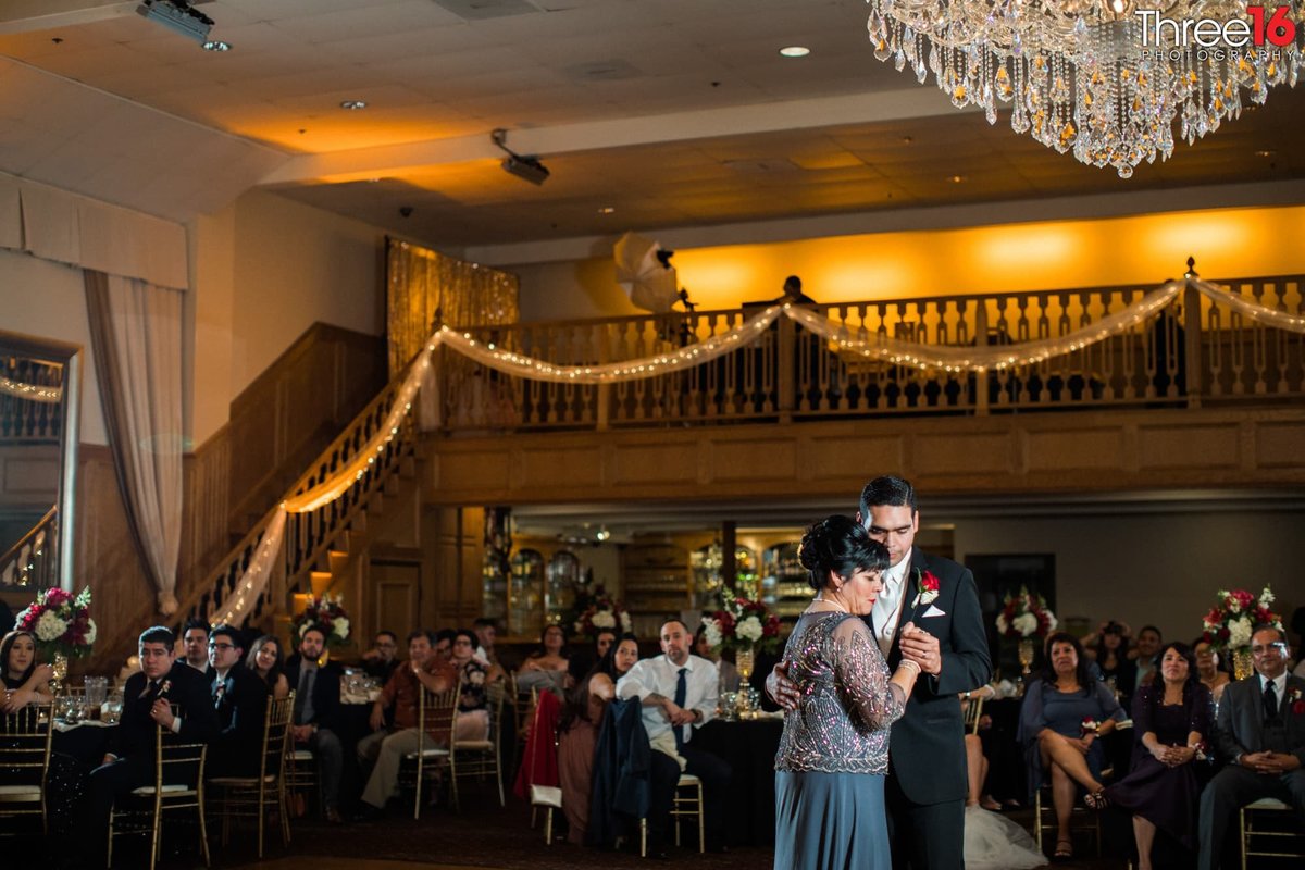 Groom dances with his mother during his wedding reception as guests look on