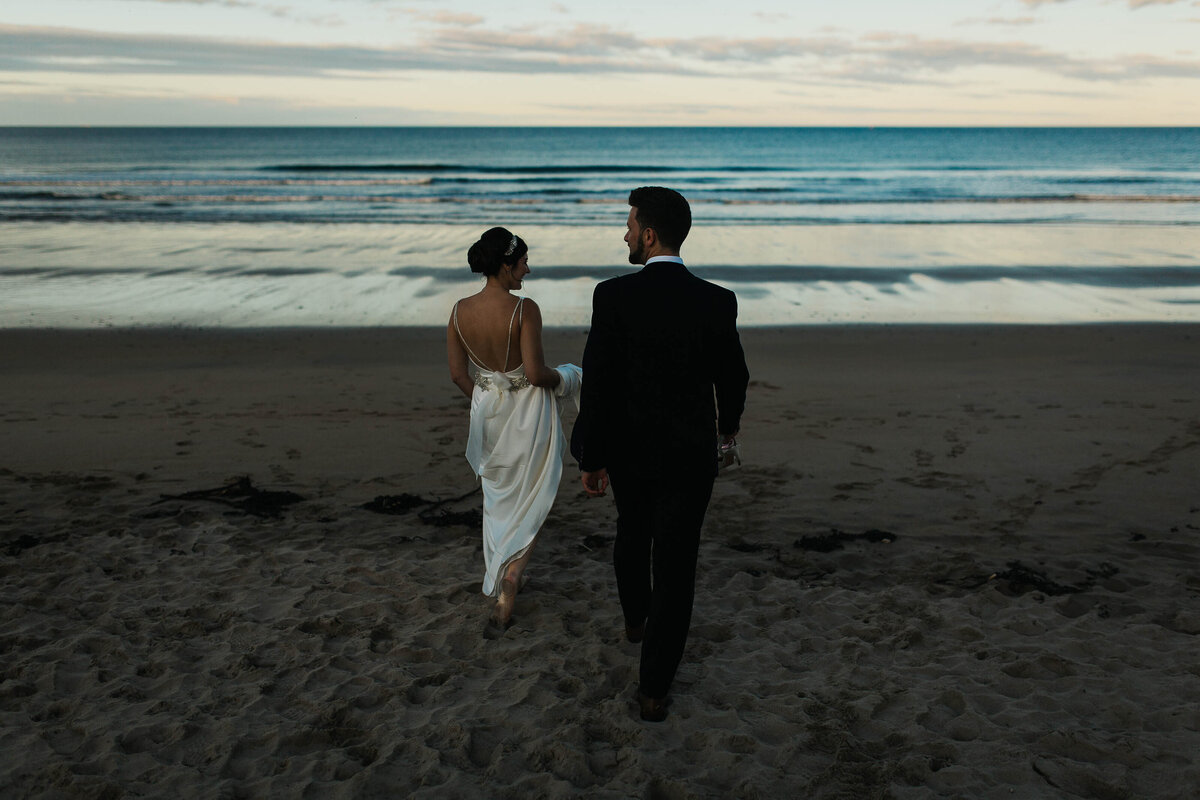Bride and groom walk onto a Northumberland beach at Blue Hour for portraits