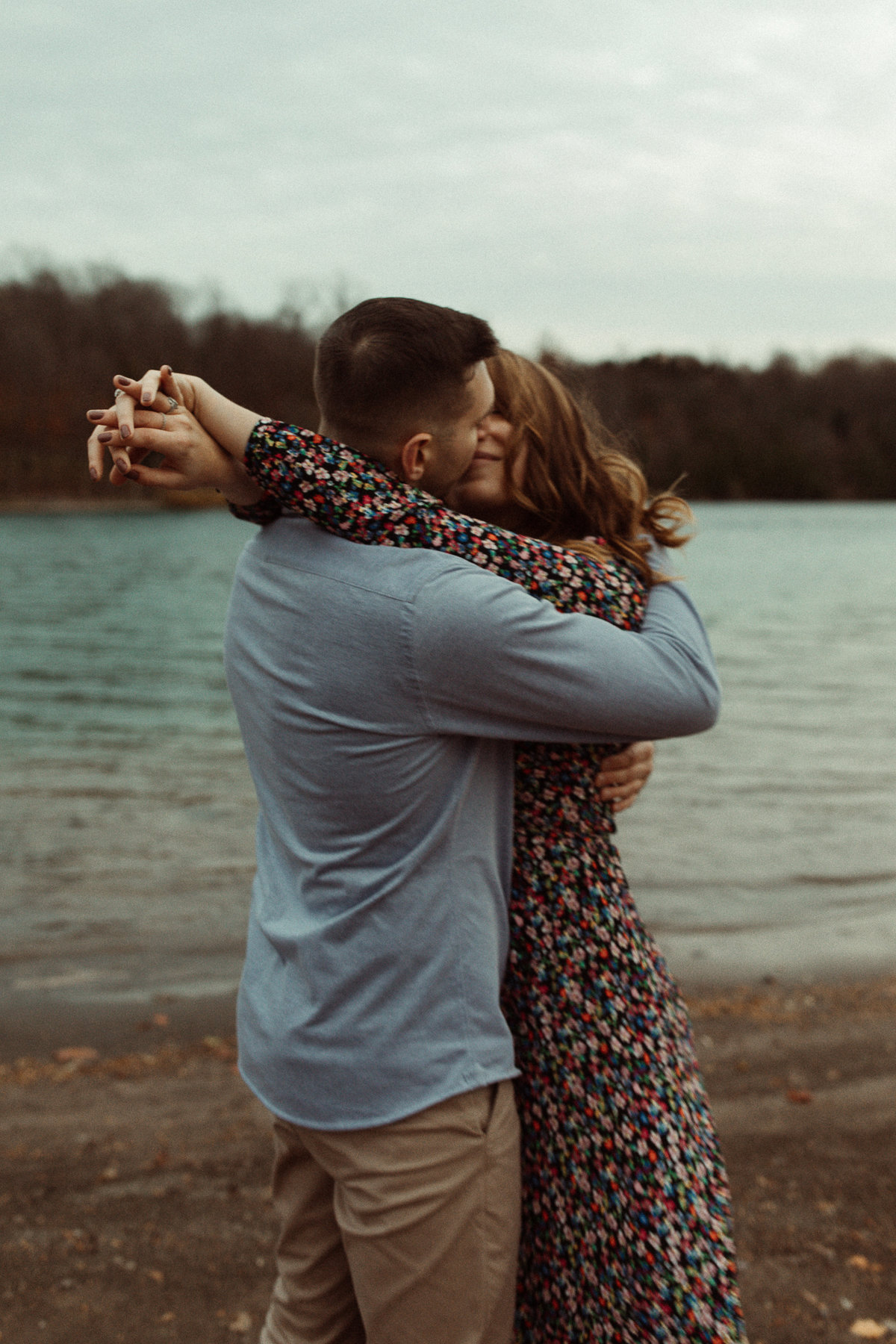 couple kisses on the beach at Green Lakes State Park. Girl is wearing a colorful floral dress