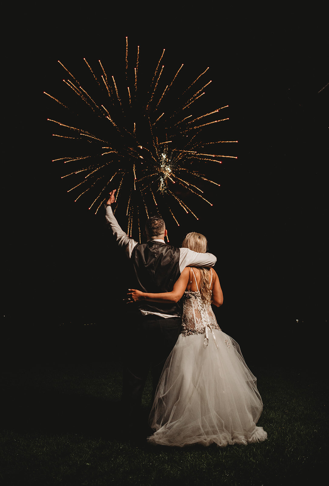 groom cheers with arm wrapped around bride with fireworks in background at wadsworth mansion wedding photo by cait fletcher photography
