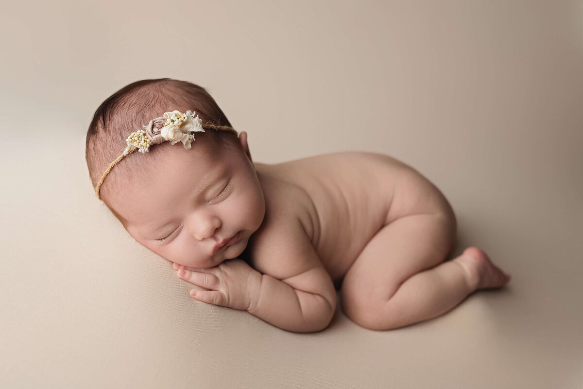 A newborn baby sleeps on a white pad with a small floral headband