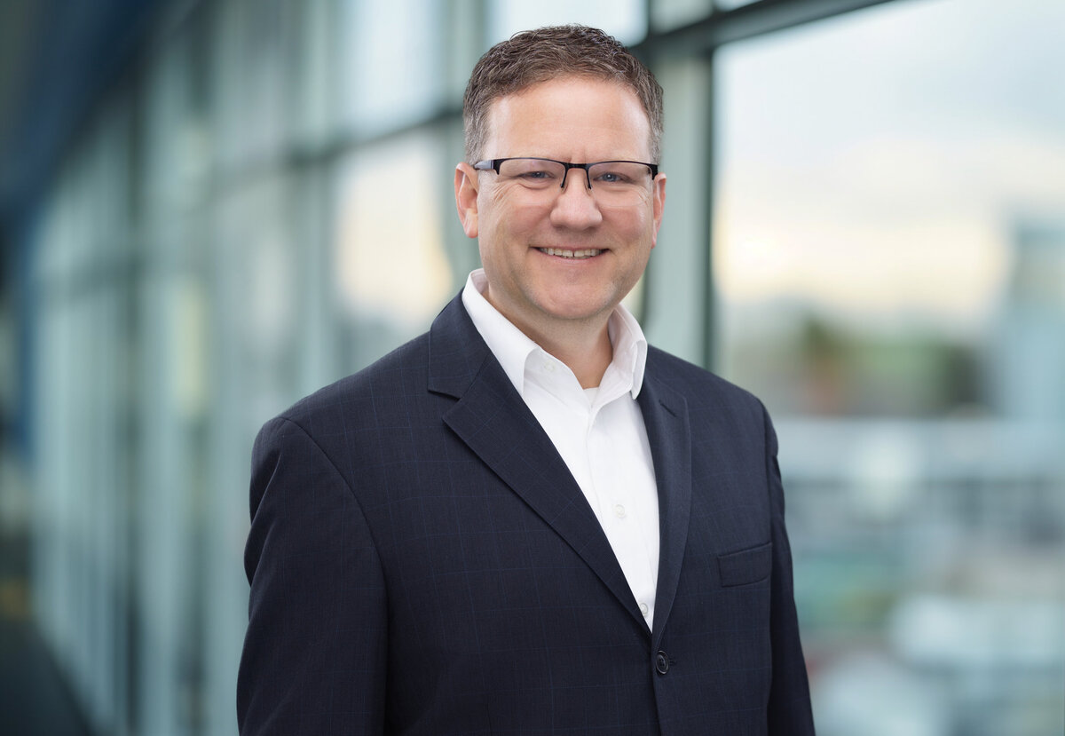 Cincinnati headshots capture a poised businessman in sharp eyeglasses and a tailored navy blazer, exuding confidence and professionalism against a contemporary glass backdrop