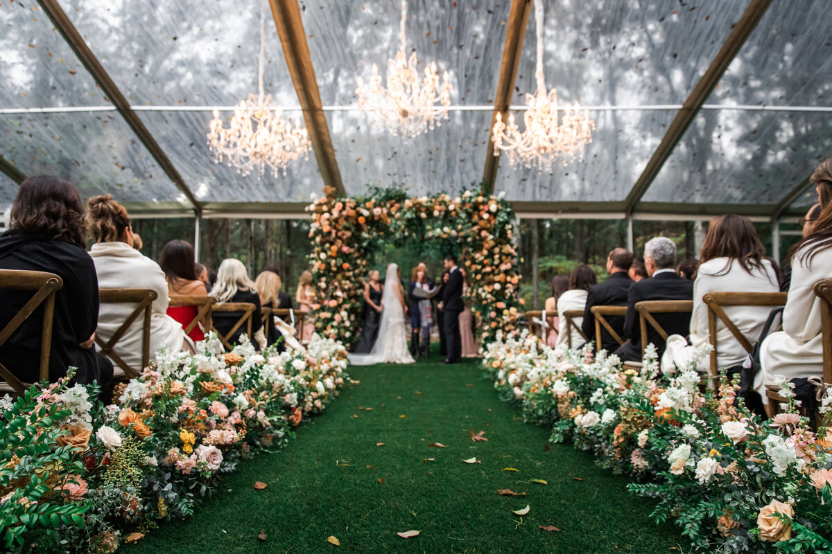 Lush floral hedges create aisle meadows for this fall wedding. Florals feature hues of terra cotta, blush, yellow, copper, and neutrals. Beautiful garden roses, dahlias, and fall florals highlight these arrangements. Design by Rosemary and Finch in Nashville, TN.