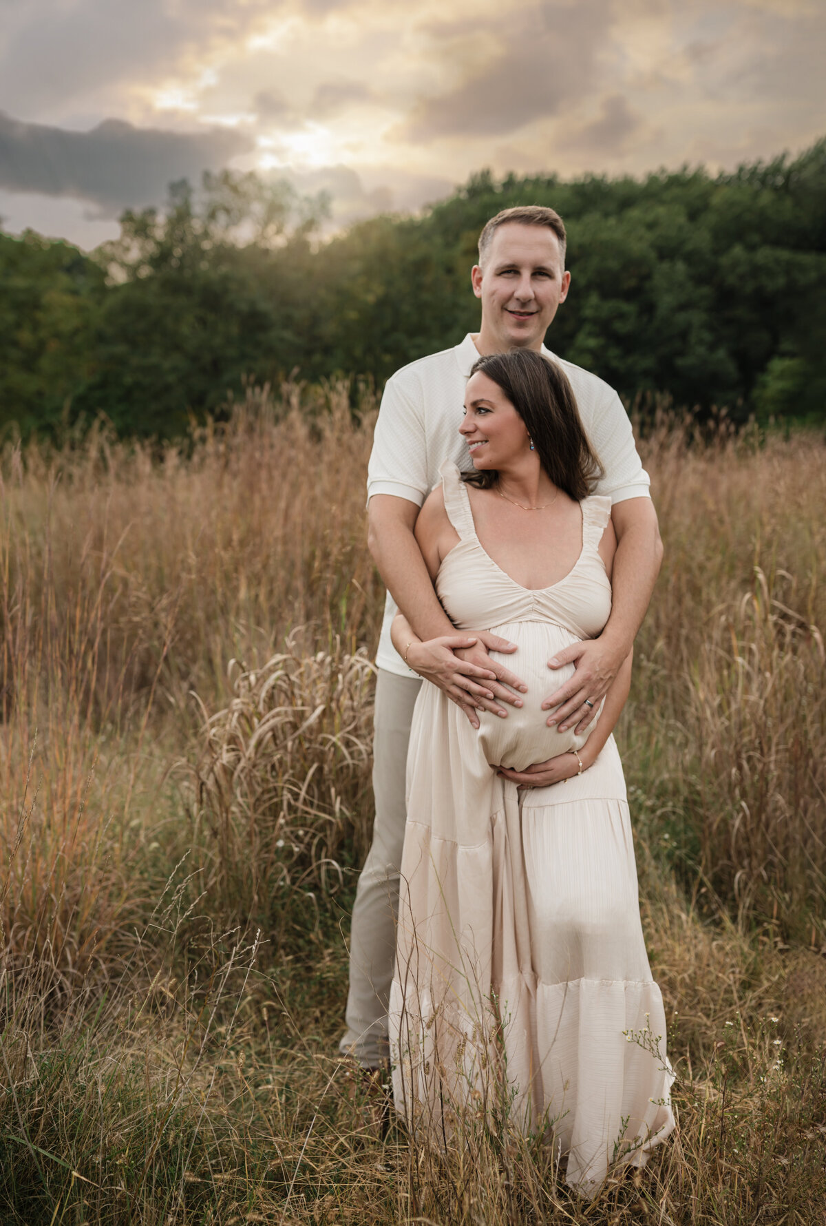 husband and pregnant wife in pink silk maternity gown holding baby bump for maternity photoshoot