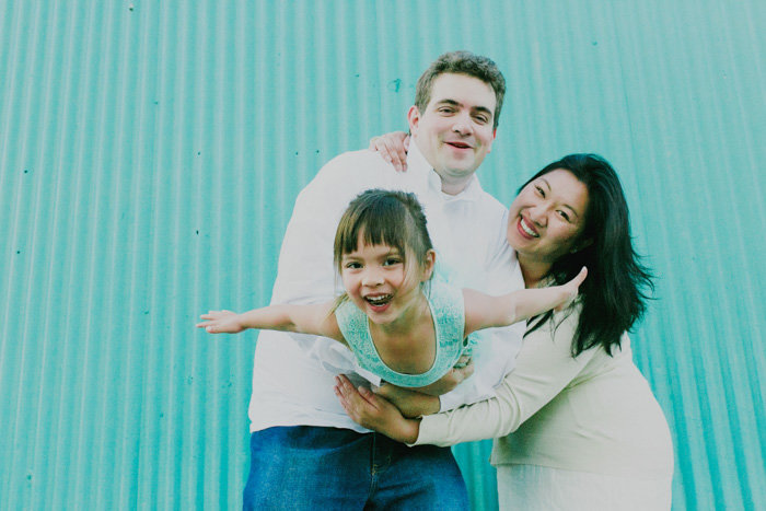 Mom and dad hold child between them smiling at the camera