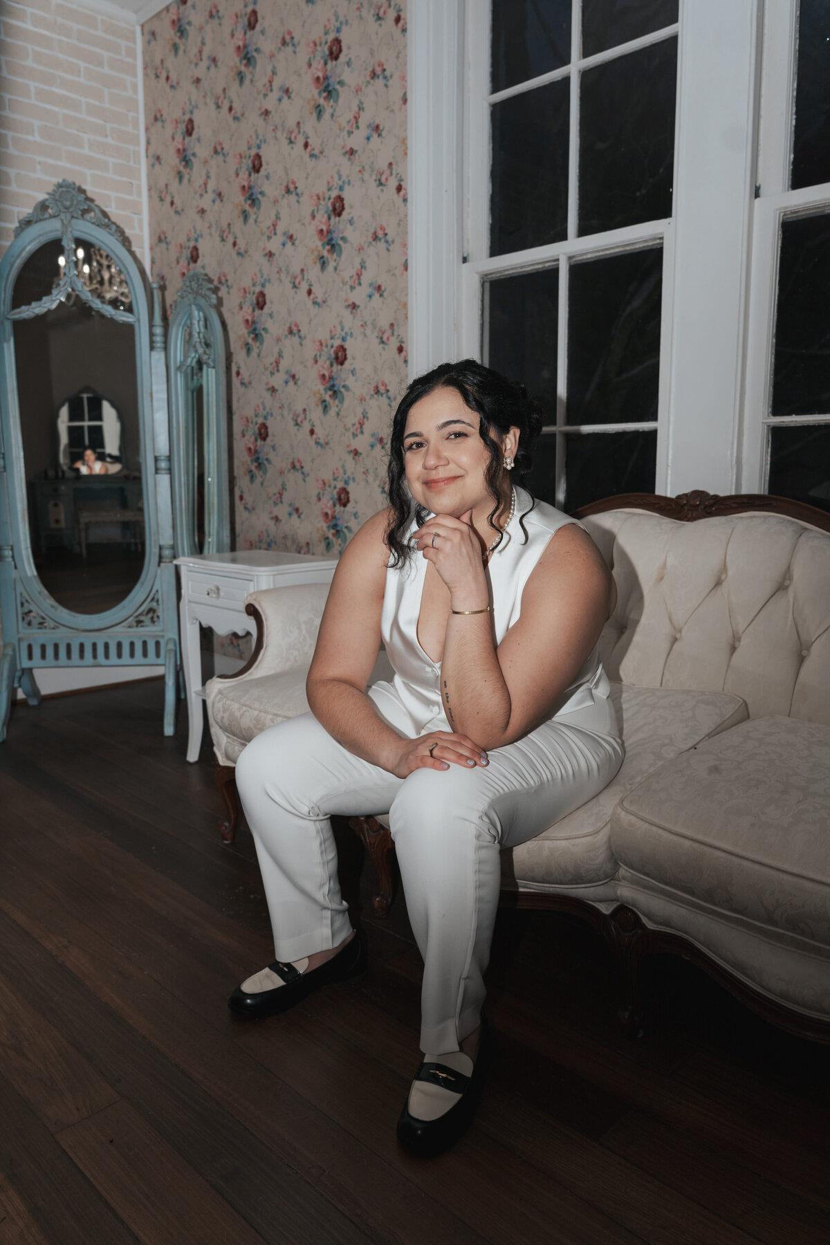 Bride rests her chin to her hand while sitting on an antique sofa 