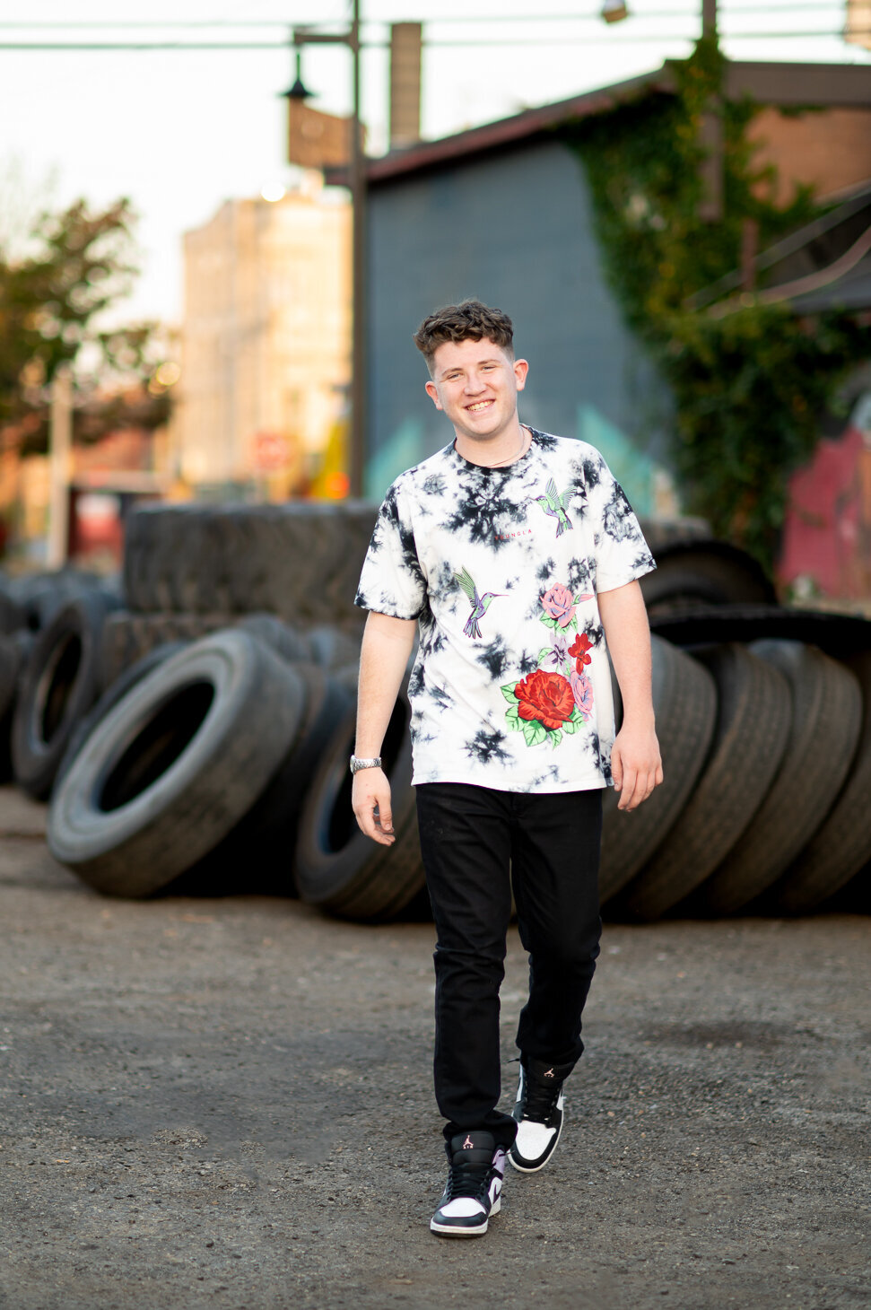 A teen boy walking in an urban area surrounded by tires and graffiti