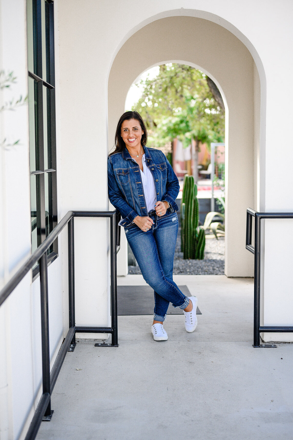 denver commercial photographer captures outdoor brand photography with woman outside on a white spansih styles building wearing denim