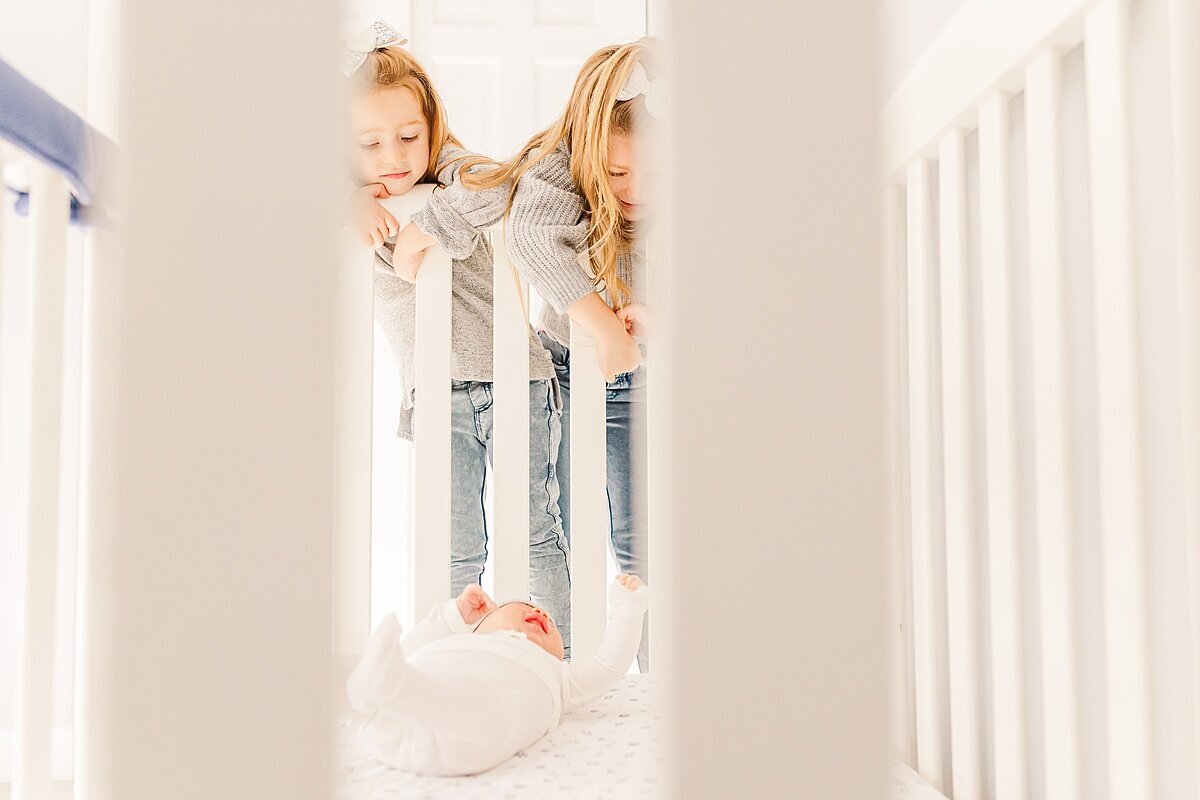 sisters look into baby crib  during in home newborn photo session with Sara Sniderman Photography in Sherborn Massachusetts