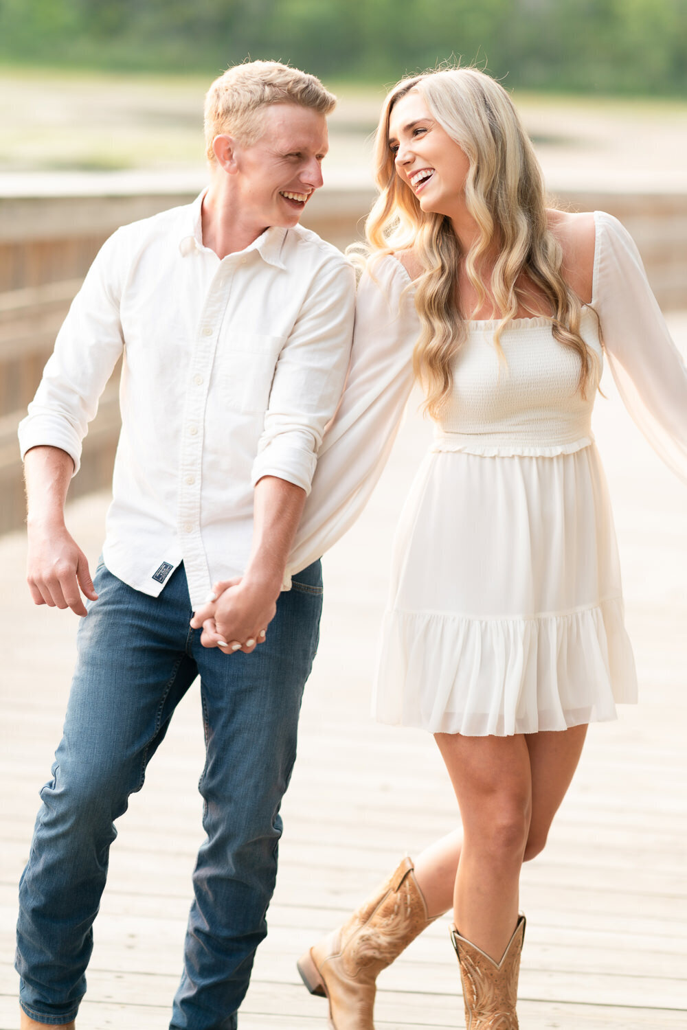 Man and woman dressed in white smile at each other while walking across a bridge.