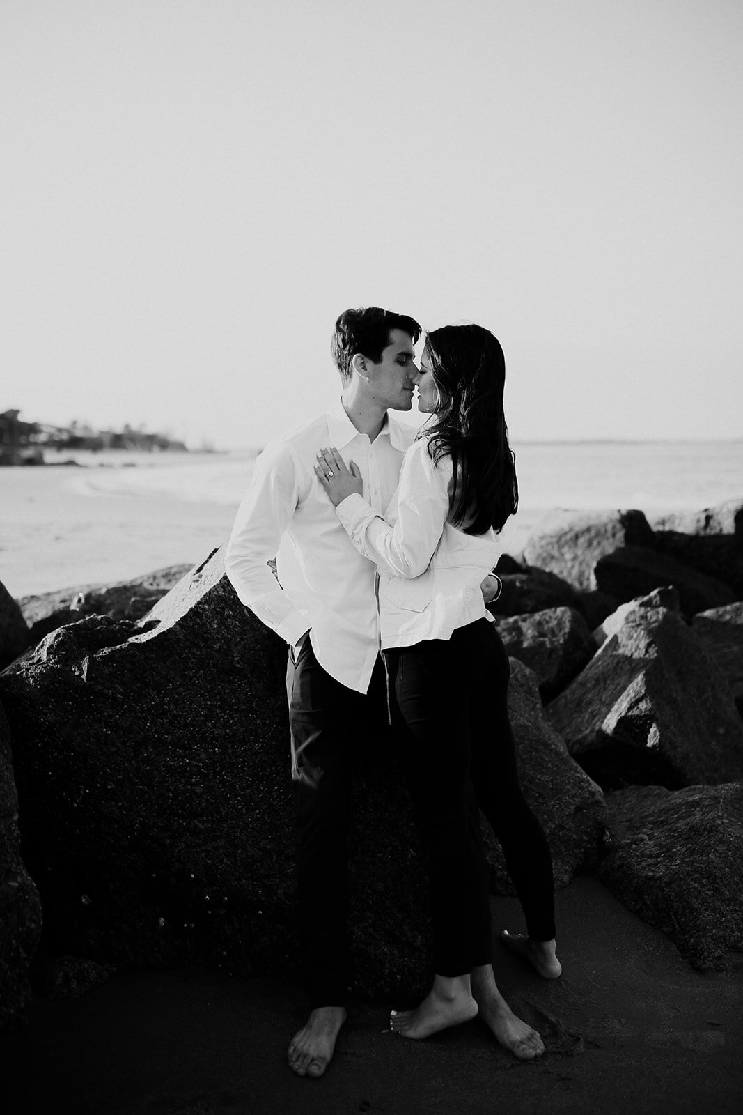 Woman kissing man leaning against rock at the beach