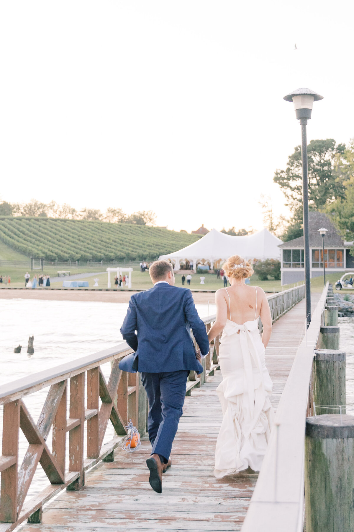 Couple running on a dock at Bohemia Overlook during their wedding day, captured in a carefree and joyful moment.