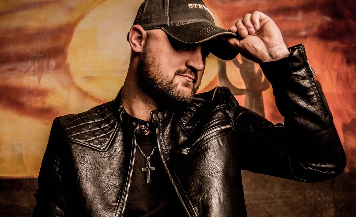 Country musician ;portrait Aaron Goodvin wearing black leather jacket holding baseball hat brim