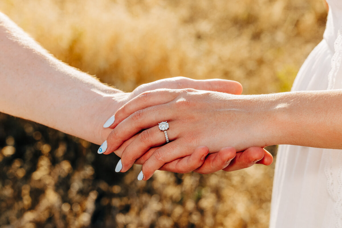 Close up engagement photo of couple holding hands with engagement ring