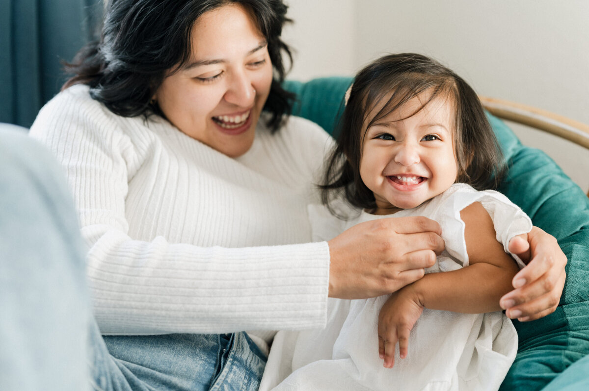 Mom plays with her little girl who is cheesing at the camera.