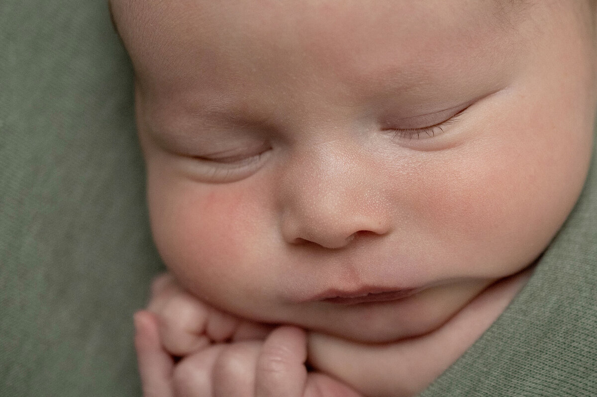 A closeup of newborn baby sleeping in green swaddle