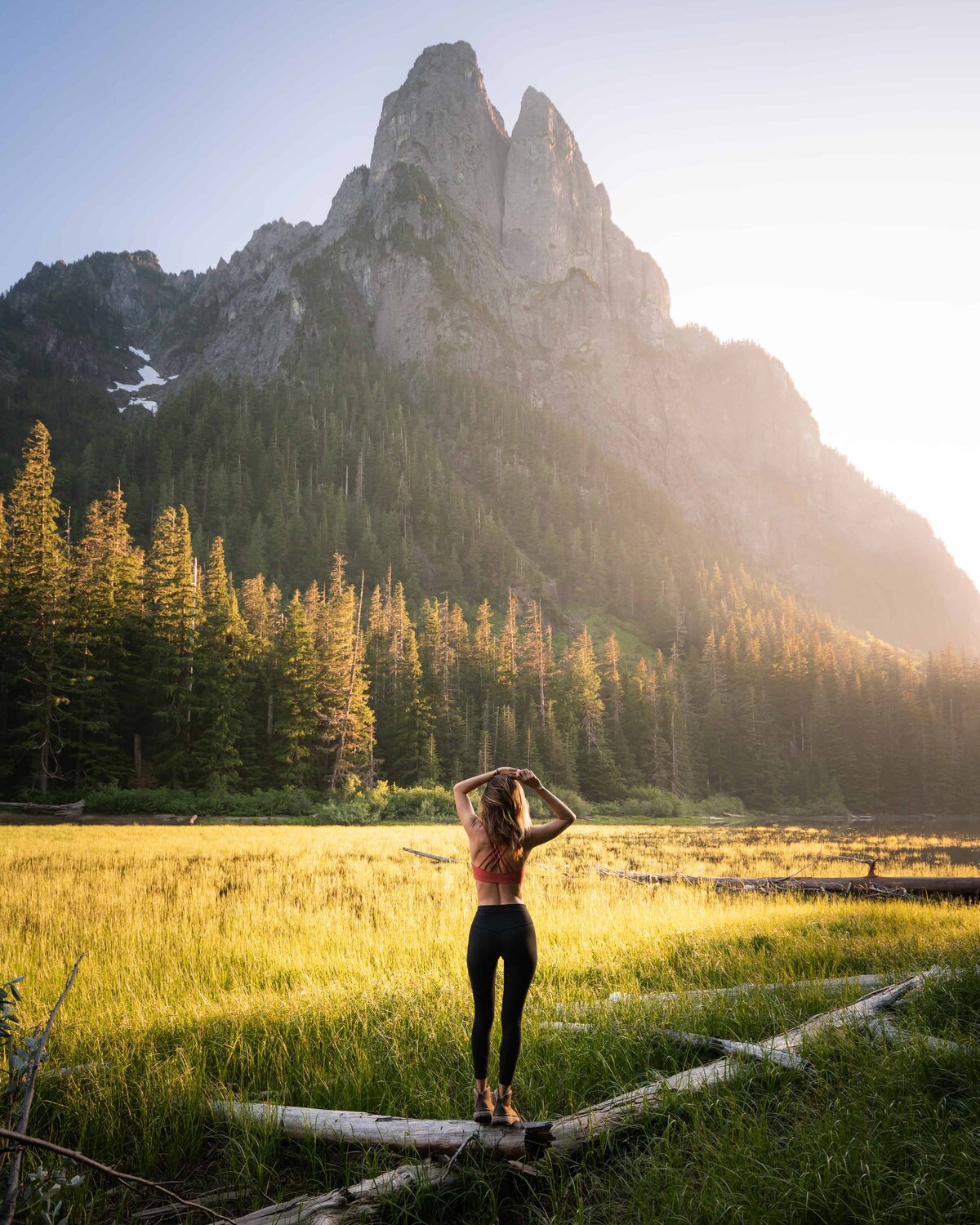 Woman standing on a log in a field of grass looking up at a mountain