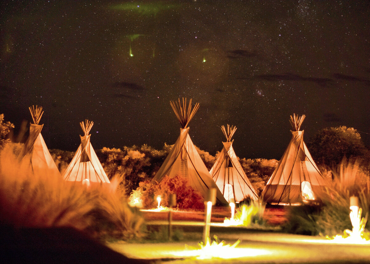 A collection of canvas tipis outdoors under a starry sky for a party.