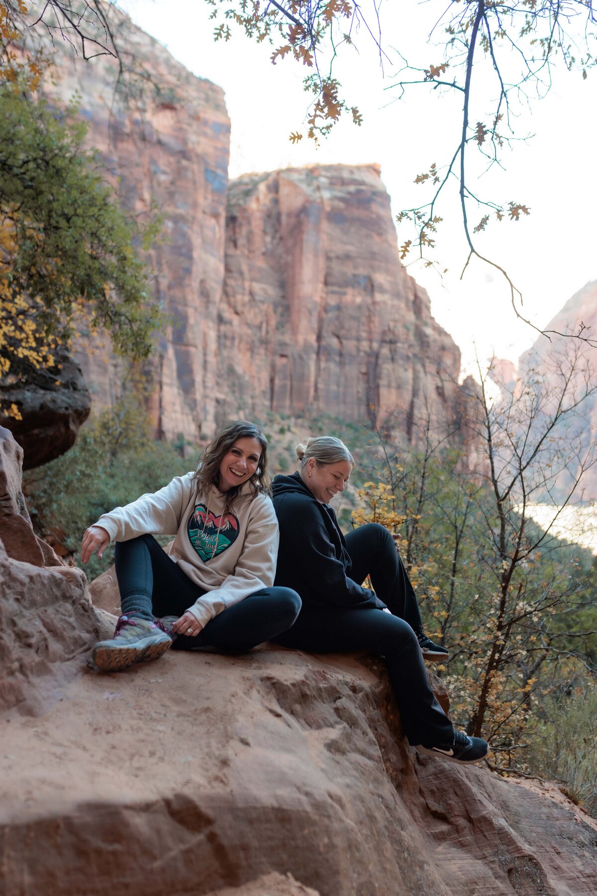 two women sitting on a boulder laughing at a joke