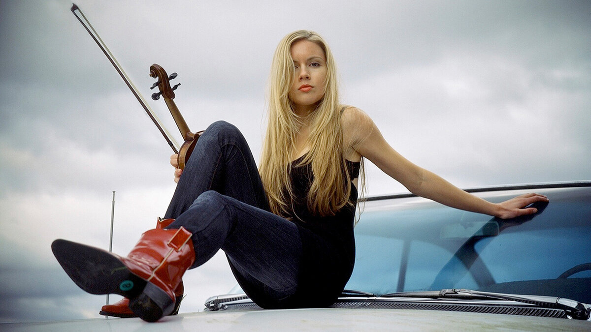 Photo country music artist Kendel Carson sitting on top of classic guitar with fiddle and red cowboy boots