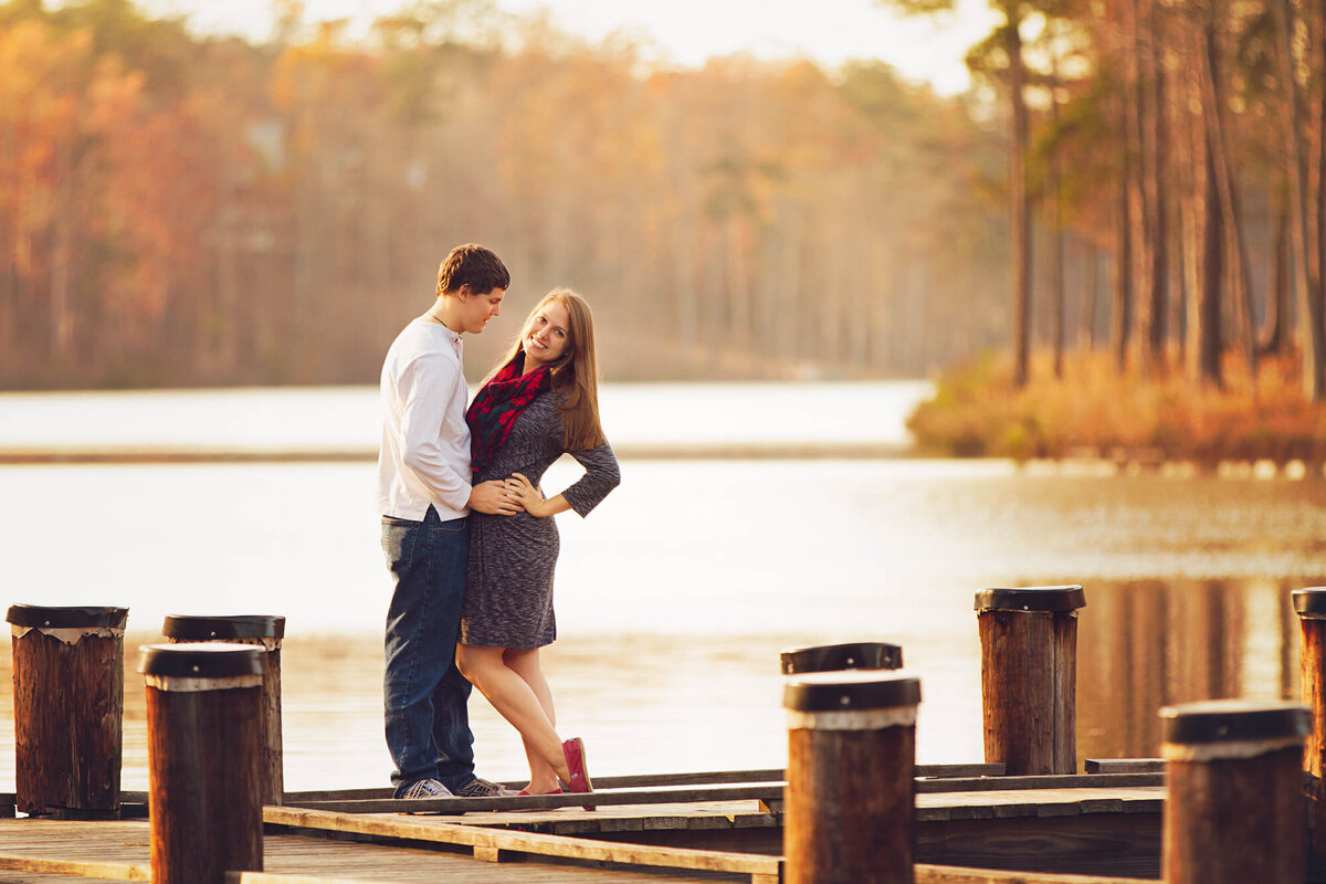 Couple cuddling while standing on the dock of Lake Peachtree at sunset.