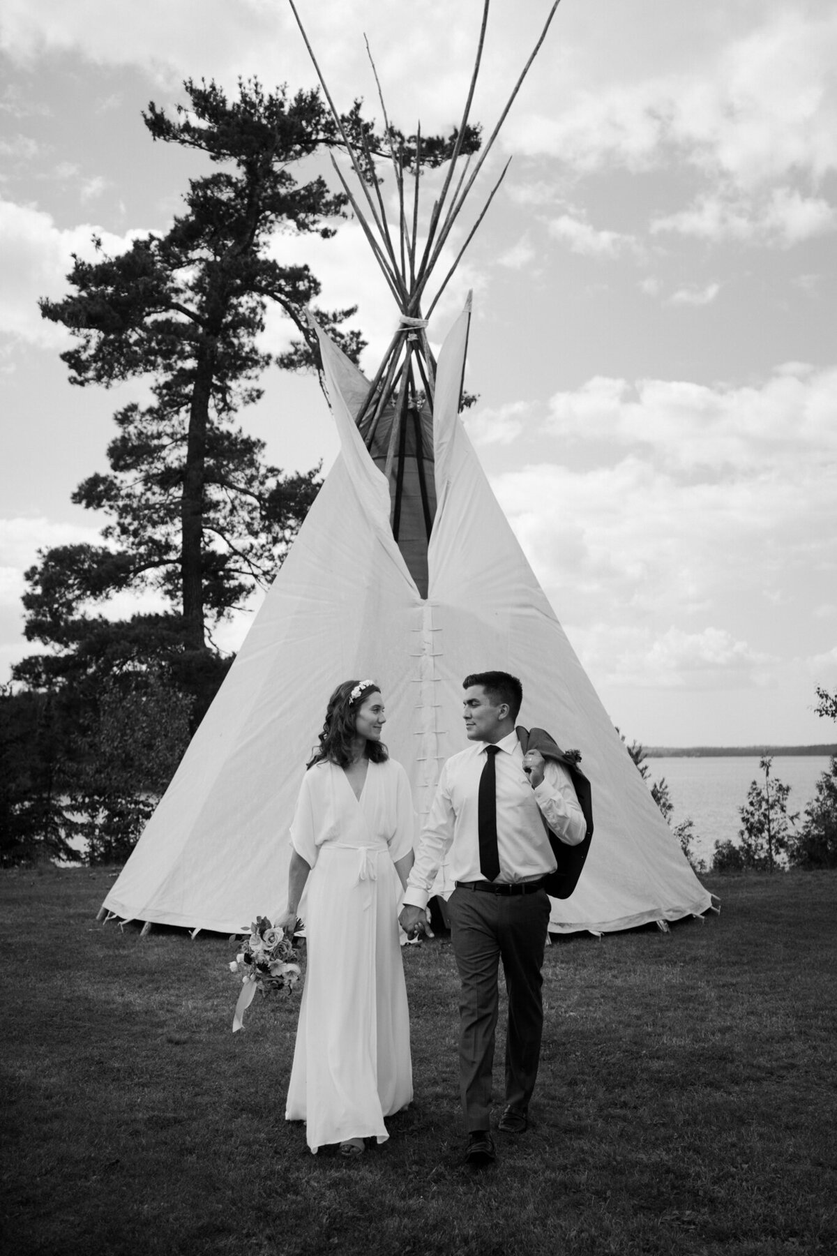 bride and groom holding hands by teepee tent