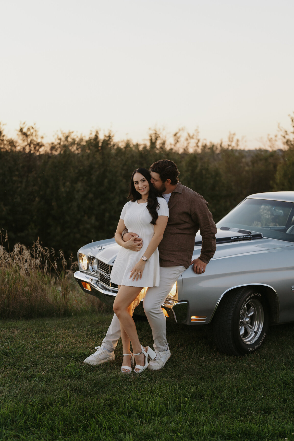 Couple poses for a photograph on the side of the road in front of their car