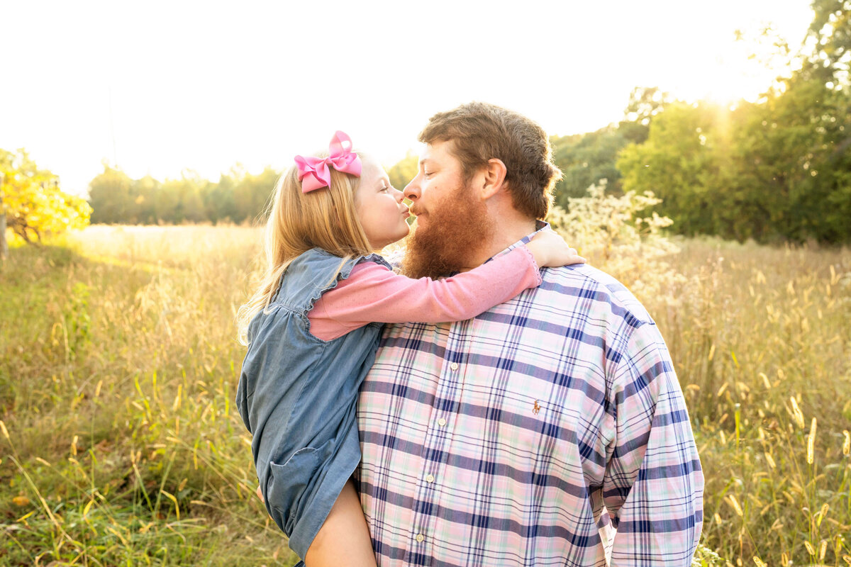 Father holding young daughter during sunset in a field of tall grass