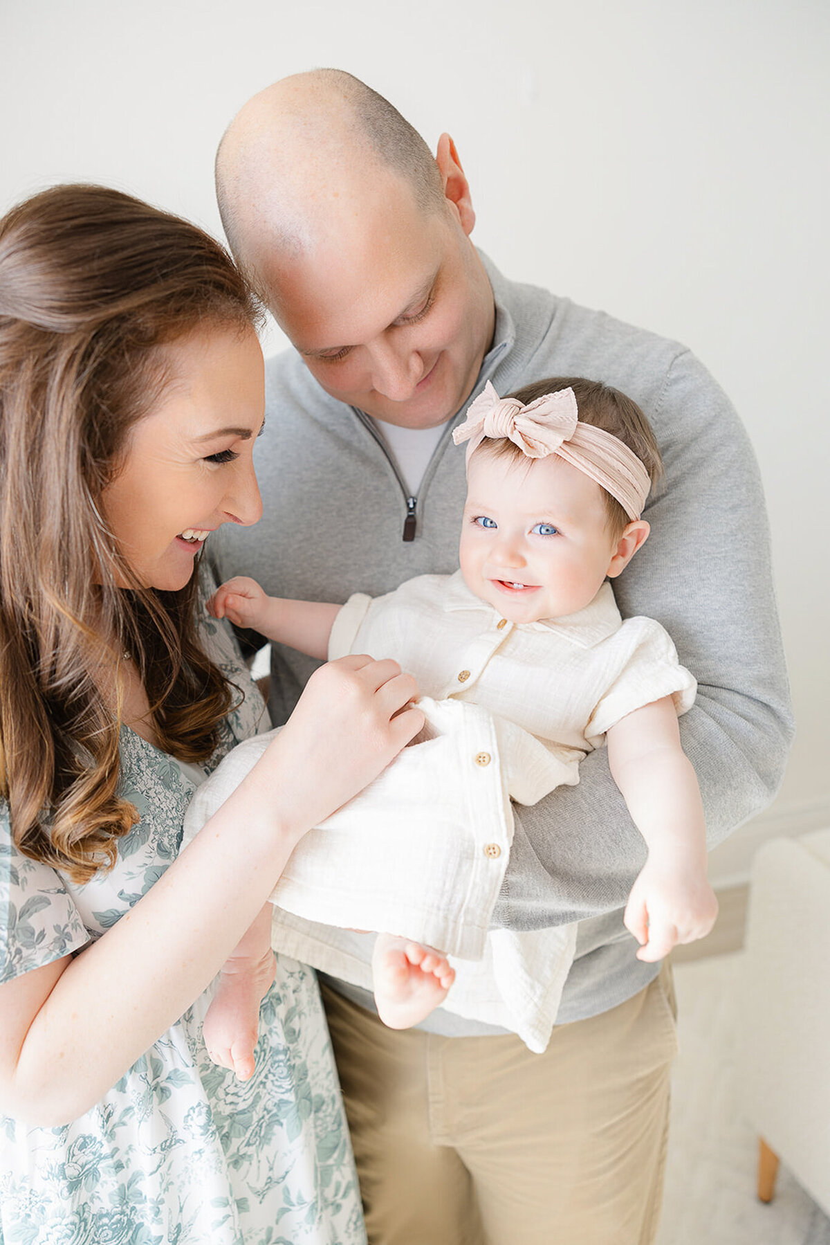 8 month old baby girl wearing pink bow smilies while being held by her parents during boston family photos