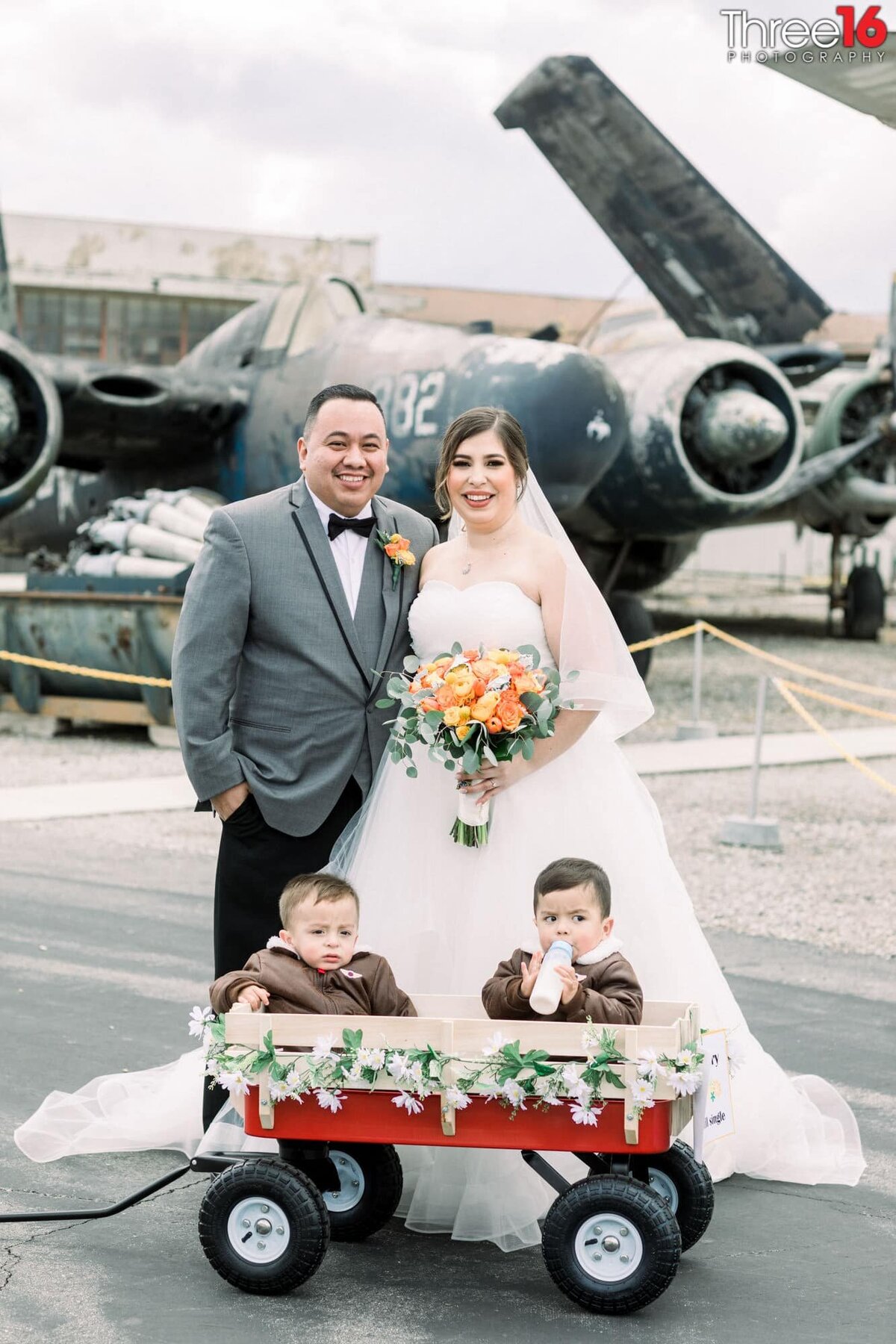 Bride and Groom pose for phots with their two sons sitting in a red wagon