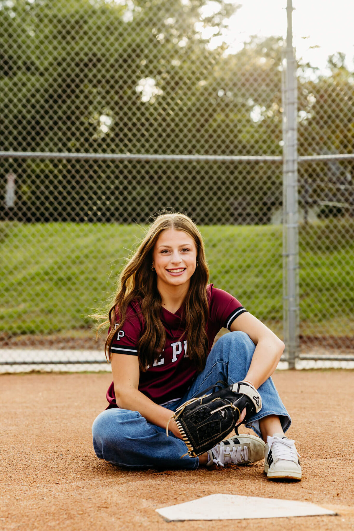 teen girl with long brown hair sitting behind home plate and wearing her softball glove at De Pere High School.