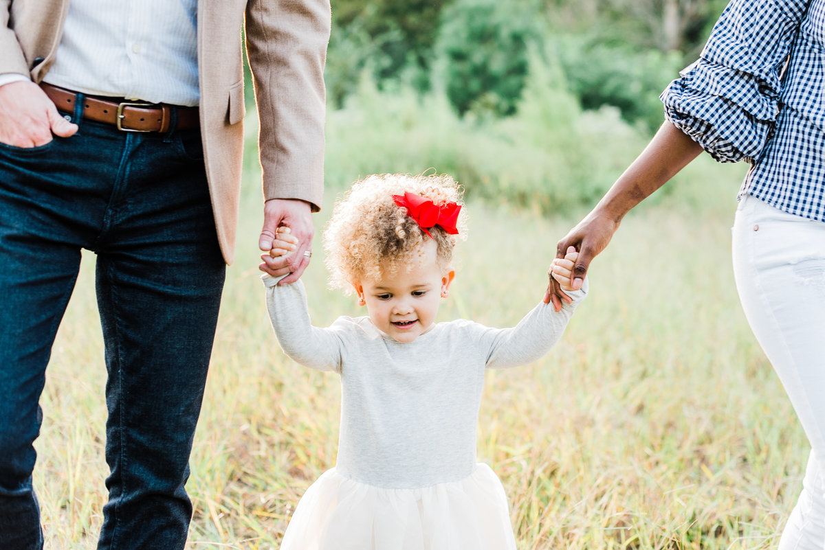 Toddler holds hands and walks with her parents during a family photo session in Raleigh NC. Photographed by Raleigh family photographer A.J. Dunlap Photography.