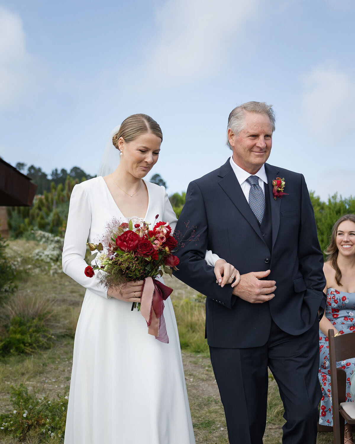 Bride holding a red bouquet walking arm-in-arm with her father