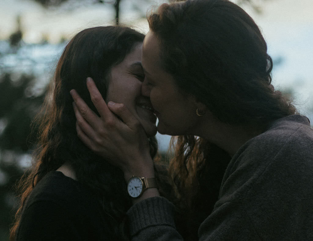 A person with their hand on their partner's face as they kiss.