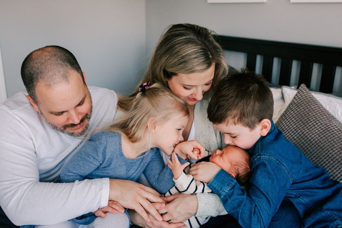 Family snuggling with new baby on their bed.