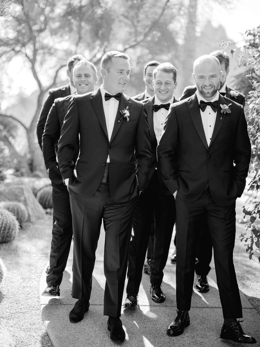 A stylish group of groomsmen in classic black tuxedos, walking with confidence and charm. The perfect wedding day aesthetic.