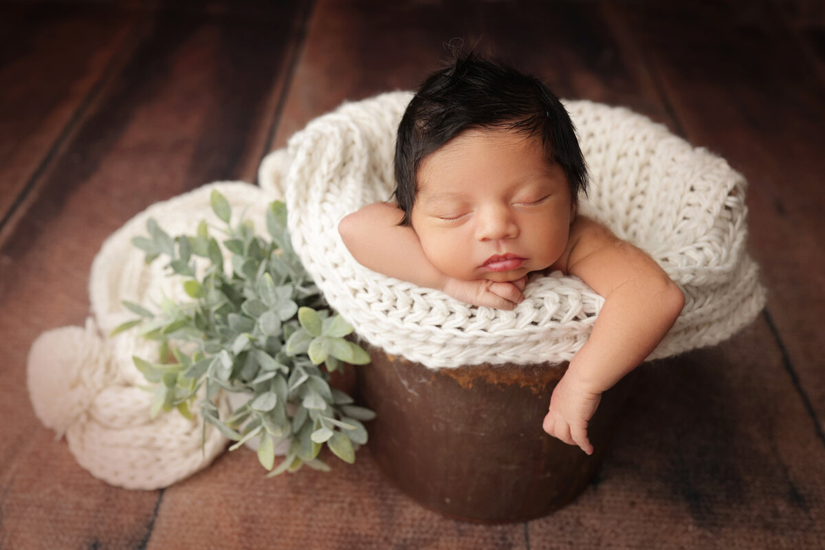 newborn boy with a lot of hair sleeping in a bucket with his arm hanging down