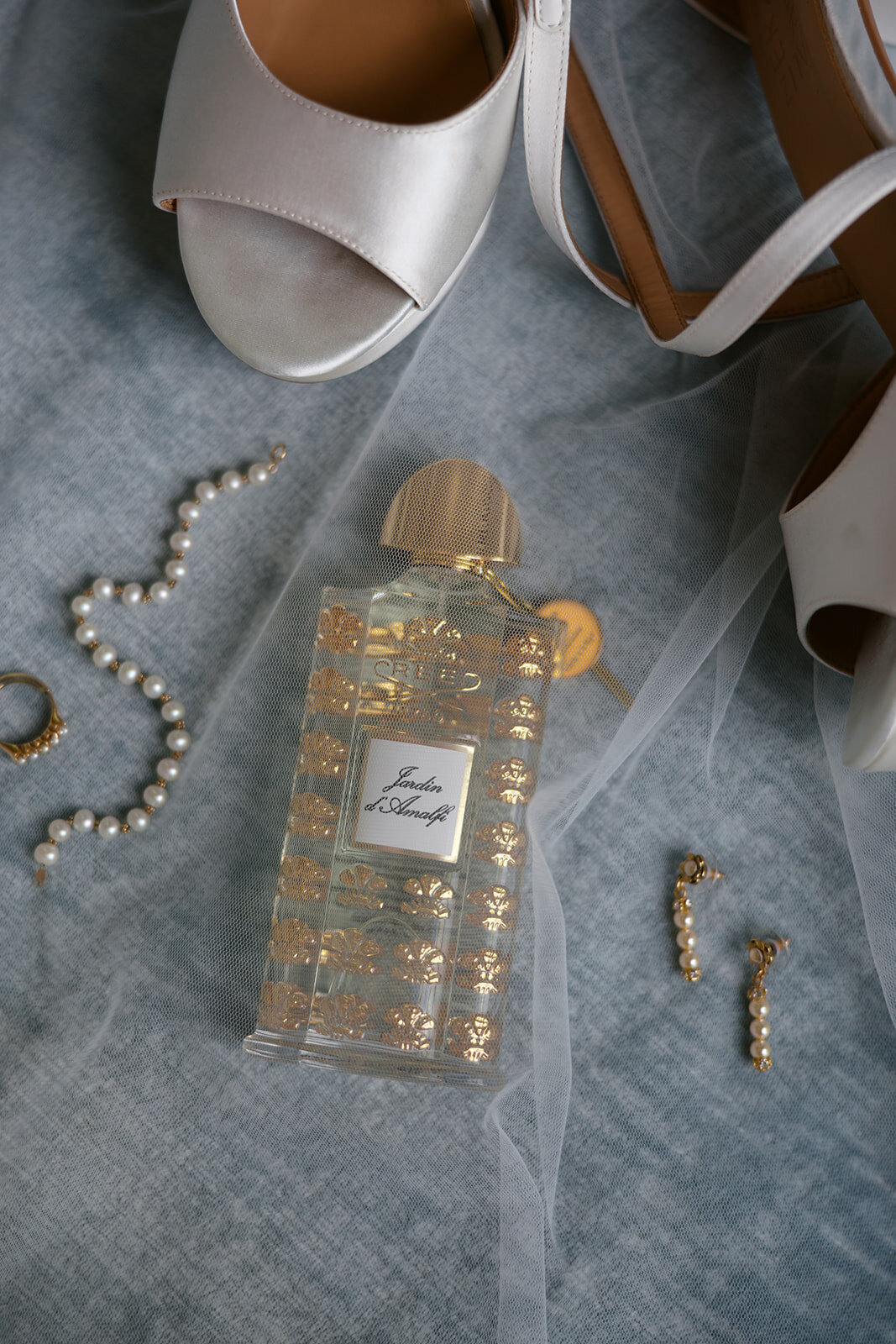 Bridal perfume bottle, pearl earrings, bracelet, and wedding ring arranged with veil in Highlands, North Carolina.