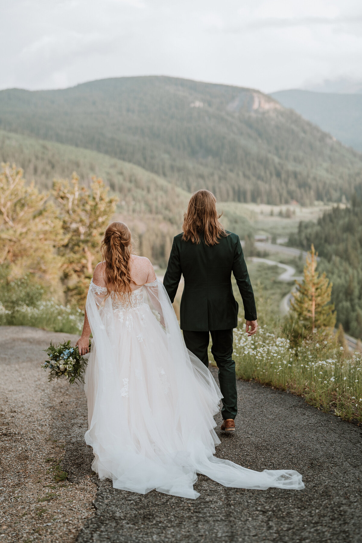 Couple walks hand in hand overlooking winding road through lush forest near Breckenridge.