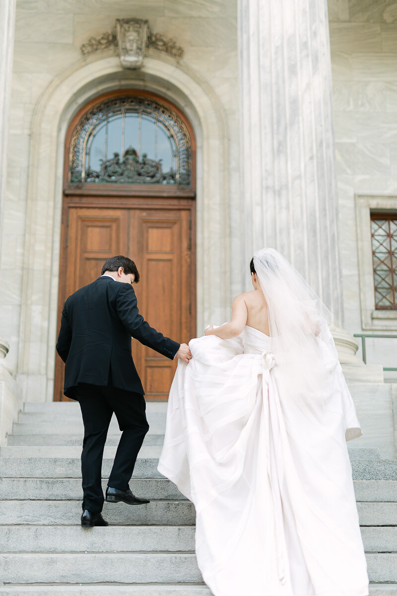 Un couple de mariés, élégants, de dos et monte les marches d'un immeuble de Montréal.