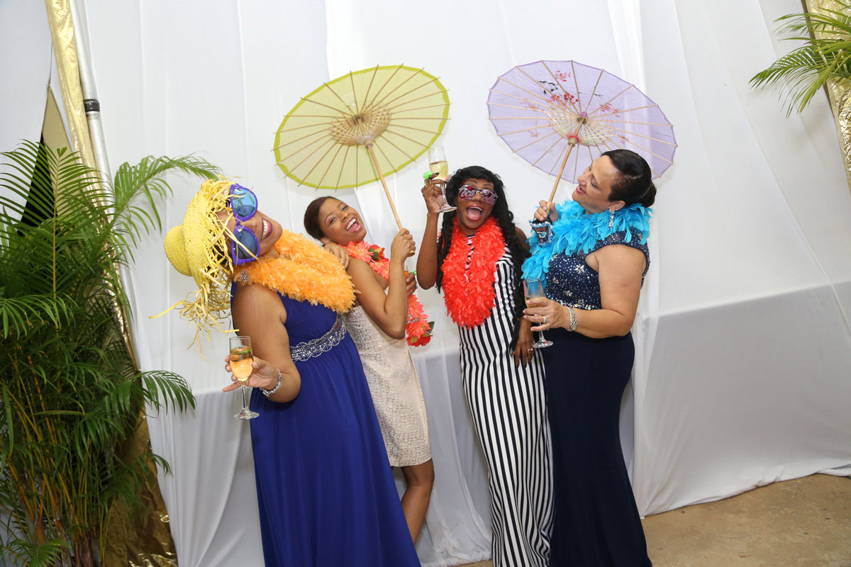 Four ladies enjoy a clean, white photobooth with boas, hats, and parasols. Photobooth by Ross Photography, Trinidad, W.I..