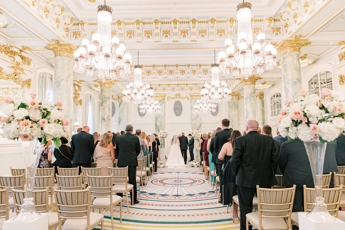 Wedding ceremony in ballroom with guests seated and chandeliers above