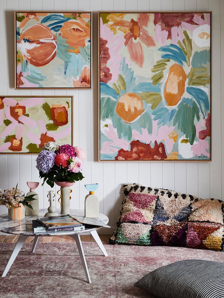 Muted floral artwork with peach and sage tones styled above a timber sideboard with books and vase
