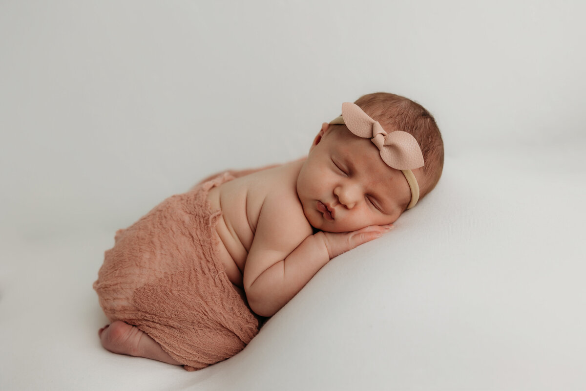 newborn baby girl on her belly , she has a pink bow head band.