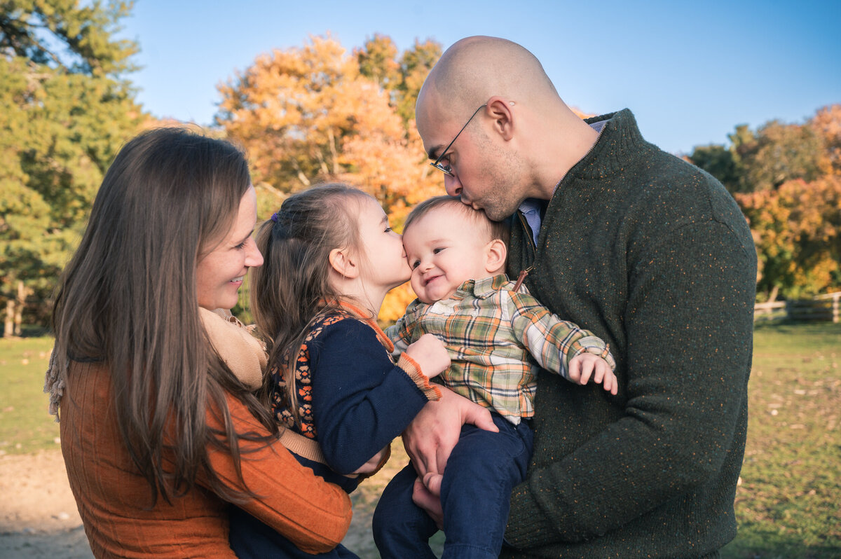 Family enjoying a photography session on a farm near Boston,  family of 4 kissing baby