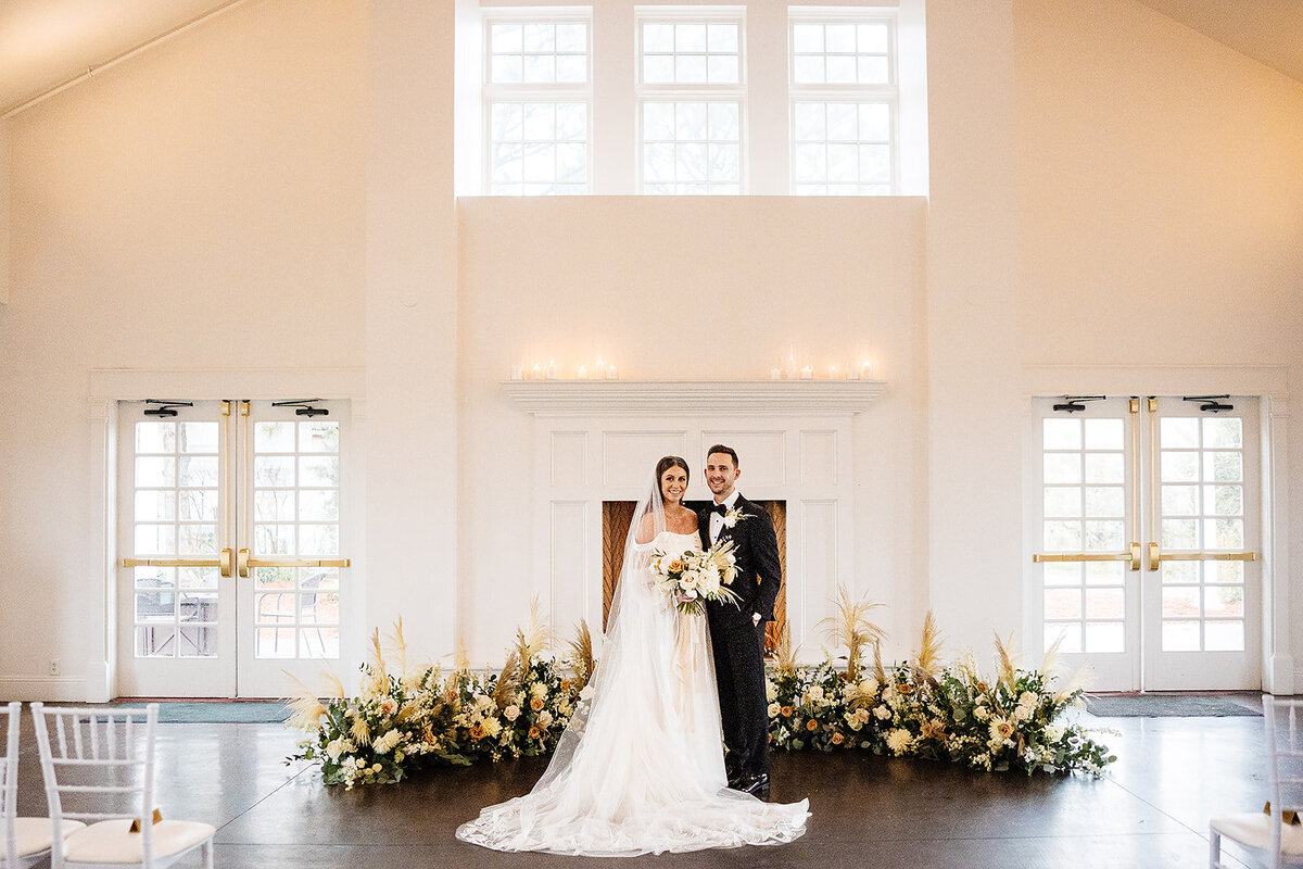 Bride and groom in front of a floral floor arch with orange flowers on their wedding day.