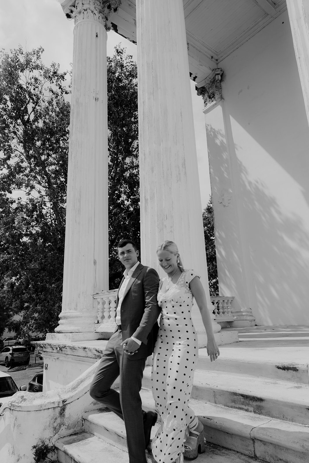 Couple holding hand walking down stairs with greel columns in background. Unique CHarleston engagement location